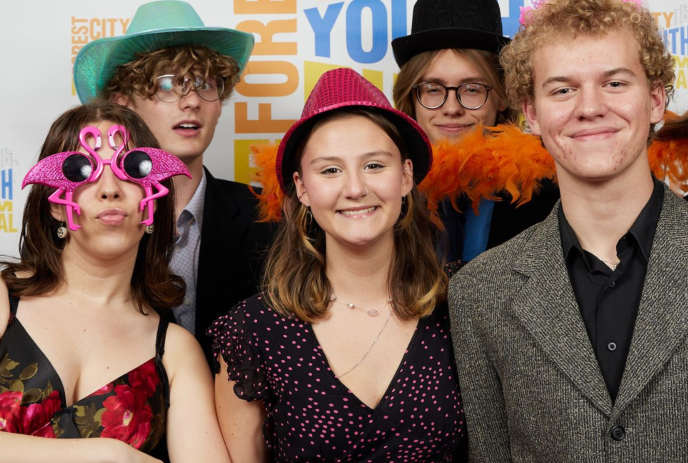 A group of people pose for a photo at an event, wearing colorful hats and accessories.
