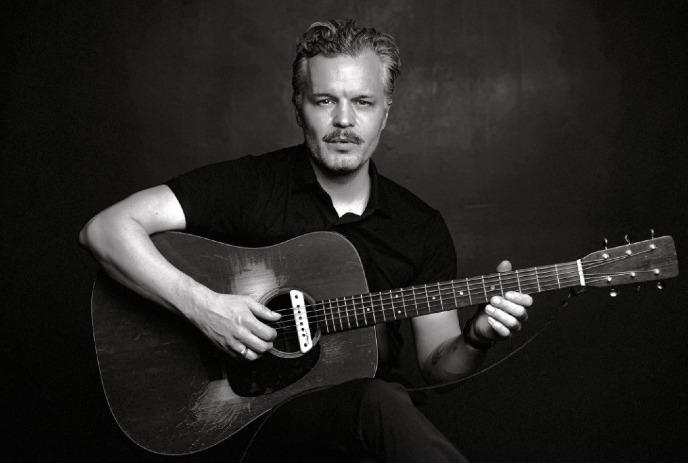 A black and white photo of Kristian Matsson, sitting down posing with his guitar.