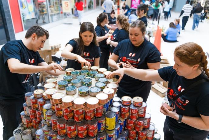 A group of people participating in a previous CANstruction London event, building a tower of cans.