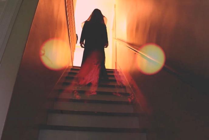 A person walks up a dark staircase towards the light.
