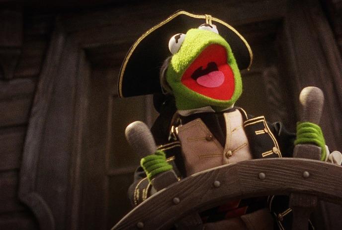 Kermit the Frog wearing an Admiral's uniform stands at a ship wheel.
