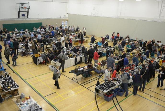 Indoor camera event in gymnasium with tables of vintage gear, people browsing, chatting, and exploring displays.