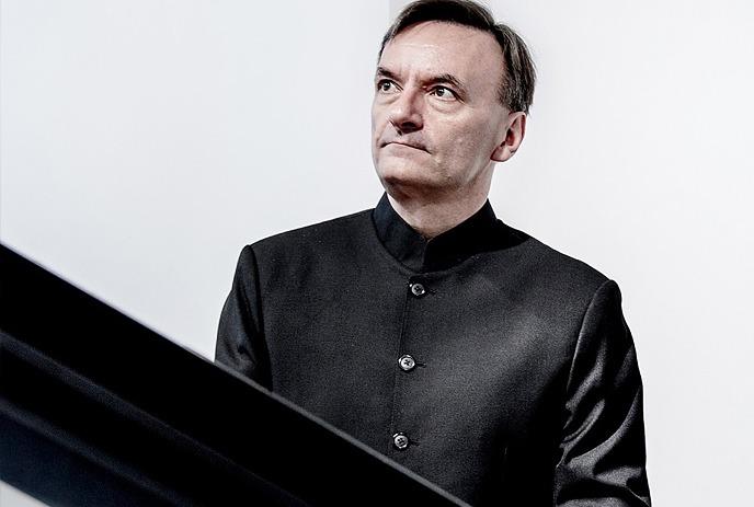 Sir Stephen Hough sitting at a piano in front of a white background.