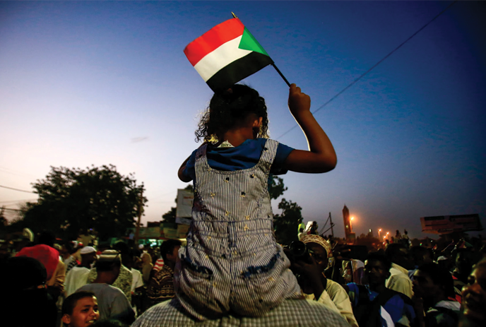 Child sitting on an adult's shoulders, waving a flag.