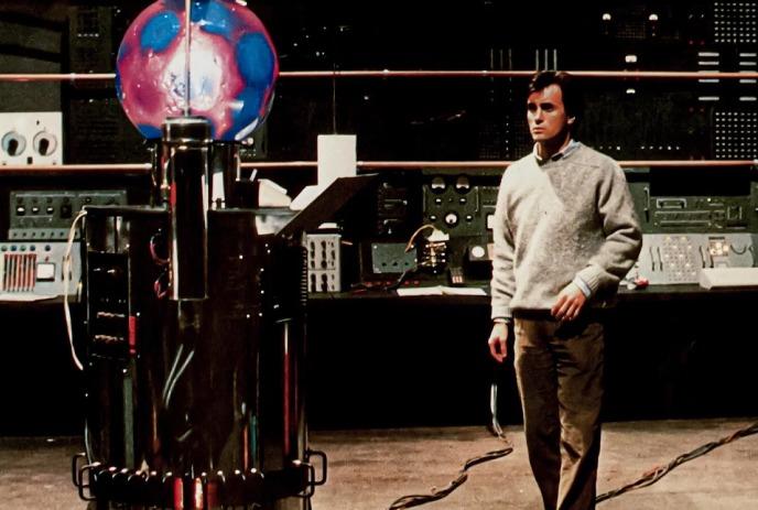 A person stands in a control room in front of a machine with a pink and blue globe on the top of it.