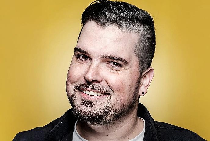 A face portrait of Mike Rita smiling warmly, with a vibrant orange background.