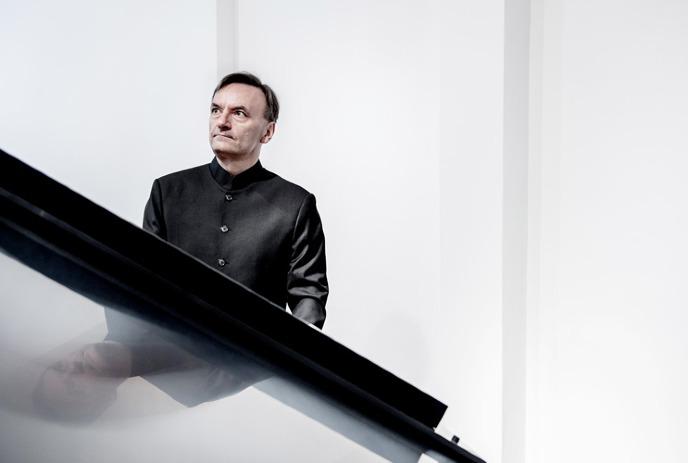Sir Stephen Hough sitting at a piano in front of a white background.