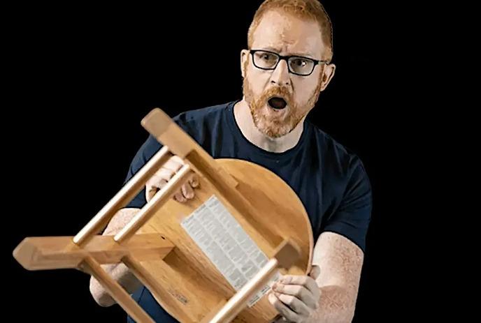A person holds a stool in front of themselves and has a scared look on their face.