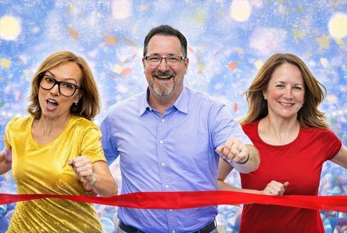 Three comedians, 2 women in a red and a yellow top and a man in blue shirt crossing a red ribbon, finishing a race.