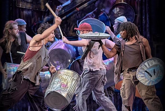 Energetic performers using trash cans and sticks as instruments in a dynamic street show.
