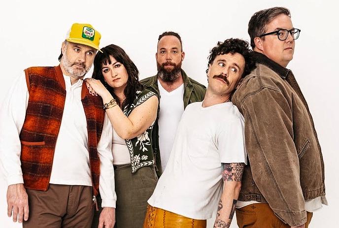 Five band members from the strumbellas posing together against white backdrop wearing varied casual outfits.