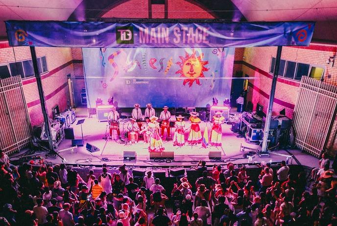 Musicians at the Sunfest stage; vibrant banner, congas, and clapping crowd radiate daytime festival joy.