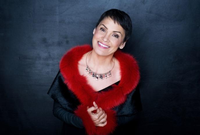Susan Aglukark looks up to the camera smiling wearing a red fur lined outfit.