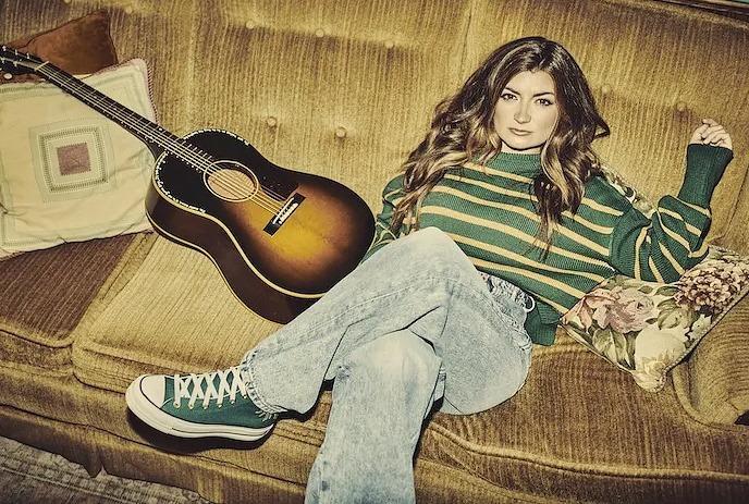 Tenille Townes sitting on her couch with her guitar, looking at the camera.