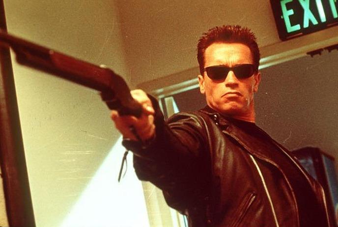 Person wearing all black and black sunglasses, pointing a gun at something out of sight.
