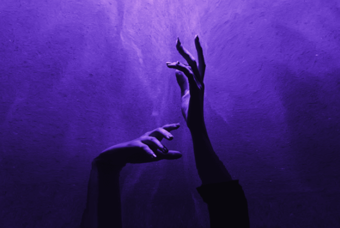 A person's hands reaching out towards a purple background.
