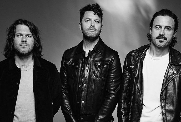 Three band members of The Fray stand in a black and white portrait. They wear leather jackets, exuding a confident demeanor.