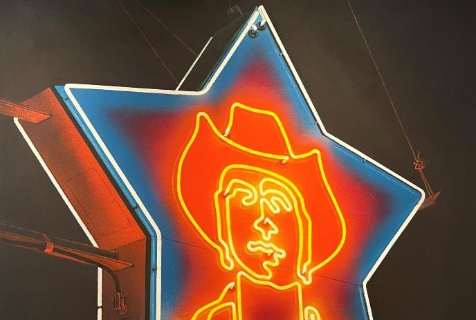 A neon sign in the shape of a five point star, with a cowboys face in the middle.