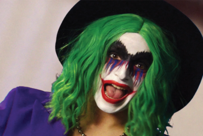 A person wearing green hair and a hat dressed as a joker.