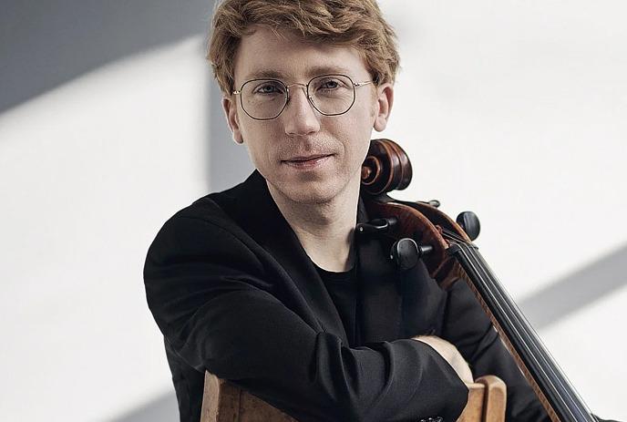 Cellist Cameron Crozman sits on a chair with his cello.