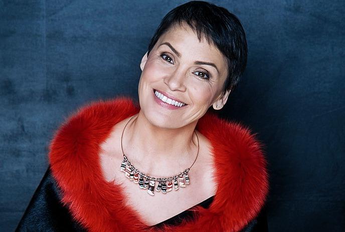 Susan Aglukark looks up to the camera smiling wearing a red fur lined outfit.