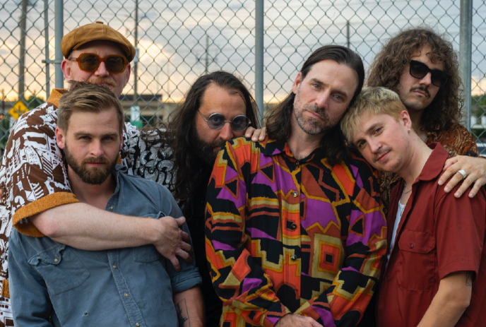 The band Golden Feather poses together in front of a chain-link fence.