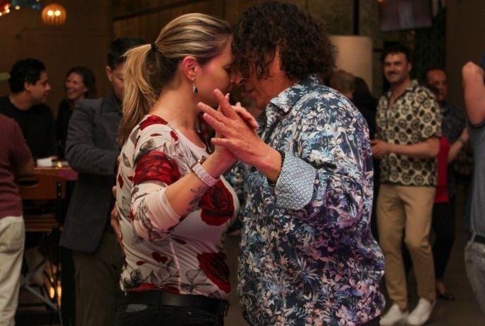 A couple dances closely at a lively Latin dance night surrounded by smiling onlookers.