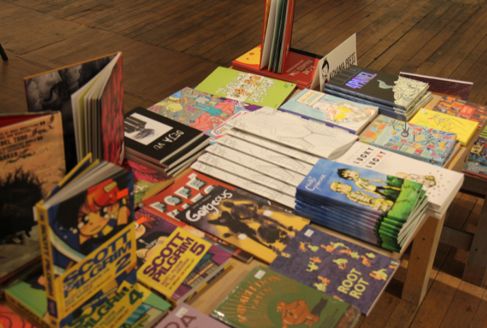 A variety of colorful comic books and graphic novels displayed on a wooden table, with titles and cover art visible.