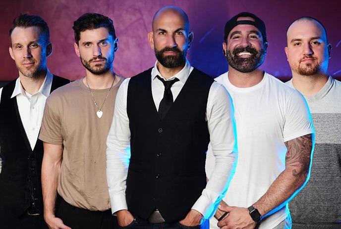 Five artists pose in monochrome style, dressed in mixed formal and casual wear, against a dramatic black backdrop.