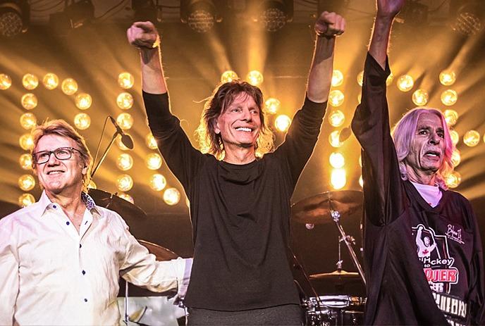 Members of the band Triumph waving to a crowd during a concert