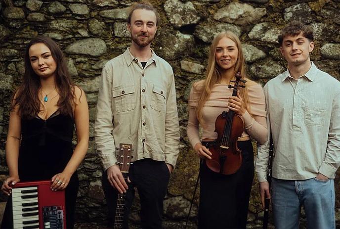 Four artists stand before stone wall holding keyboard guitar violin while fourth stands calmly completing ensemble.
