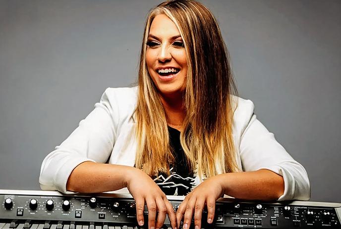 Artist Laura Gagnon with long hair in a white blazer against a gray background.