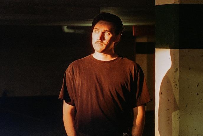 Willem James Cowan standing with his hands in his pockets, in an underground parking garage with no cars.