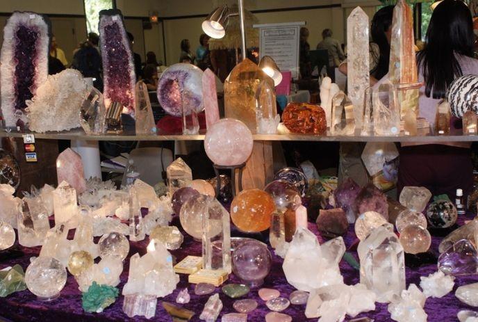 Table filled with polished and raw crystals arranged neatly with people browsing in a bright indoor market