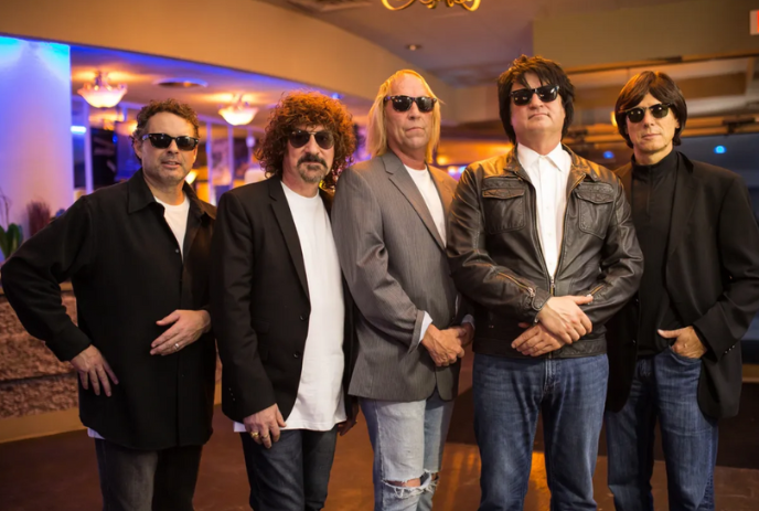 Group of band members standing together all wearing black sunglasses.