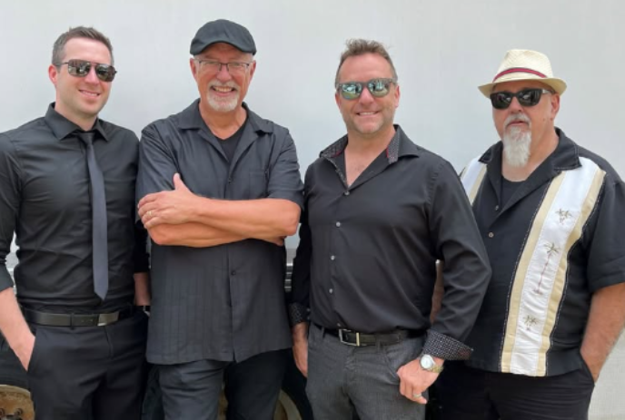 Four band members dressed in mostly black, stand together for a group photo.