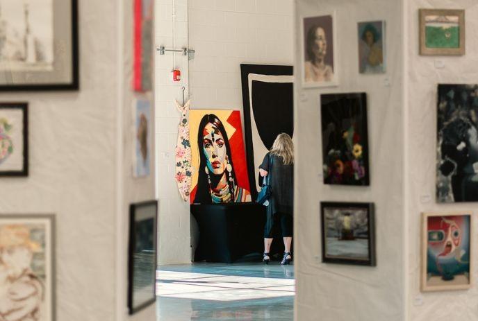 A large, colorful painting of a stylized figure and other framed artworks displayed in an illuminated gallery.