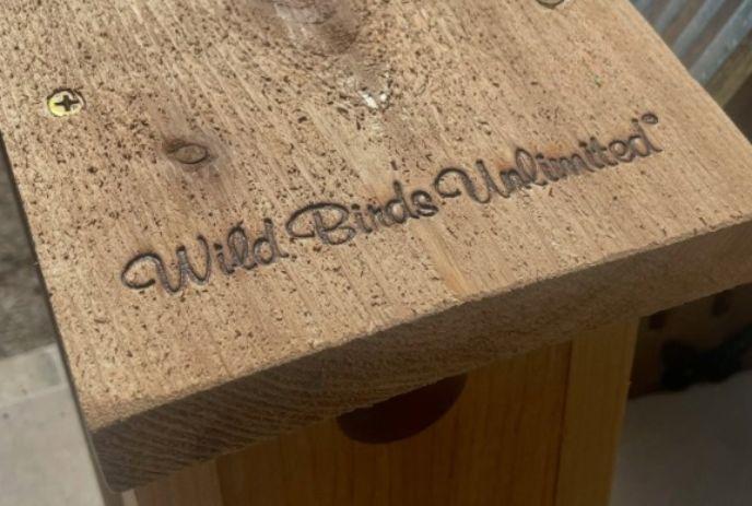 Wooden birdhouse roof engraved with the logo 'Wild Birds Unlimited' in cursive text.