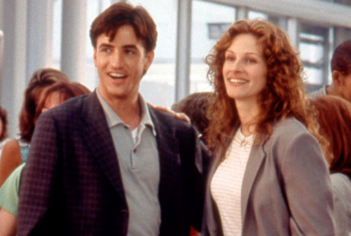 Two people standing close together in a crowd of people, smiling.