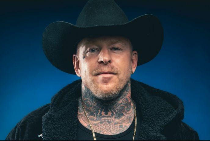 A stylish individual with black cowboy hat and a plush fur-lined jacket, complemented by a gold chain necklace.