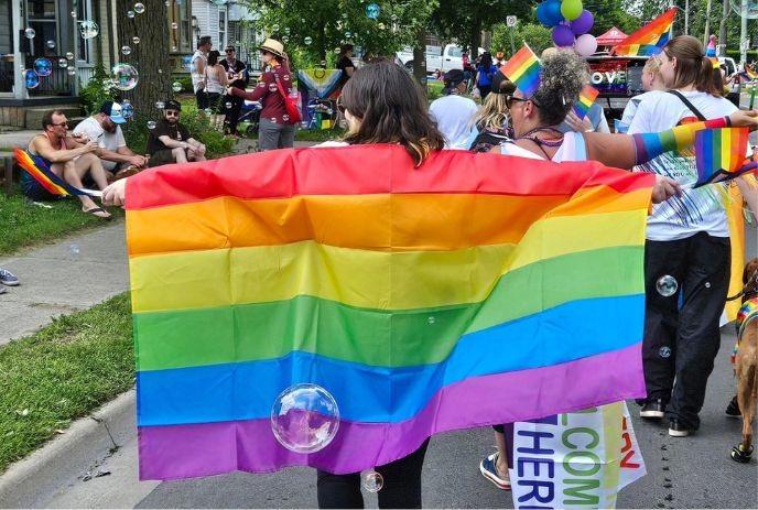 Pride parade scene with a rainbow flag waving, joyful crowd, colorful bubbles floating, and vibrant LGBTQ+ celebration.