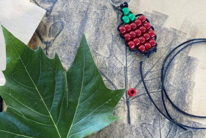 Green leaf, strawberry keychain with beads, red bead, and black string on paper with leaf prints.