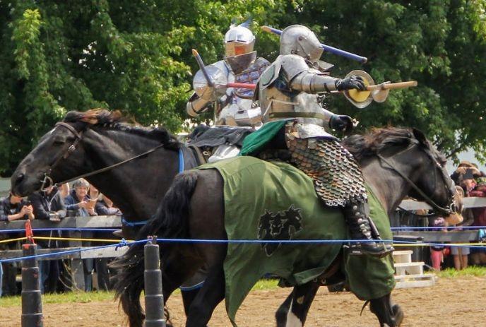 Two armored knights clash mid-joust on horseback, one lance striking a shield in dramatic medieval reenactment.