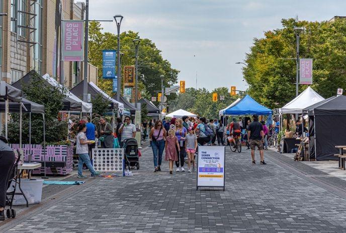 A bustling street market with various stalls, people walking, shopping, and interacting under bright sunlight.