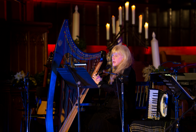 Loreena McKennitt playing a harp onstage with candles behind her.