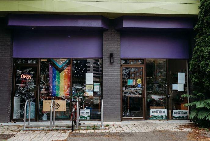A rainbow flag and signs decorate a store with a parked bike—boldly inclusive storefront.