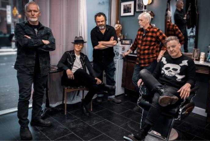 Five older men posing in a stylish barbershop, dressed in casual and rocker-style clothing.