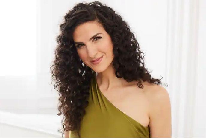 Laila Biali smiling wearing a green dress, in front of a white background.