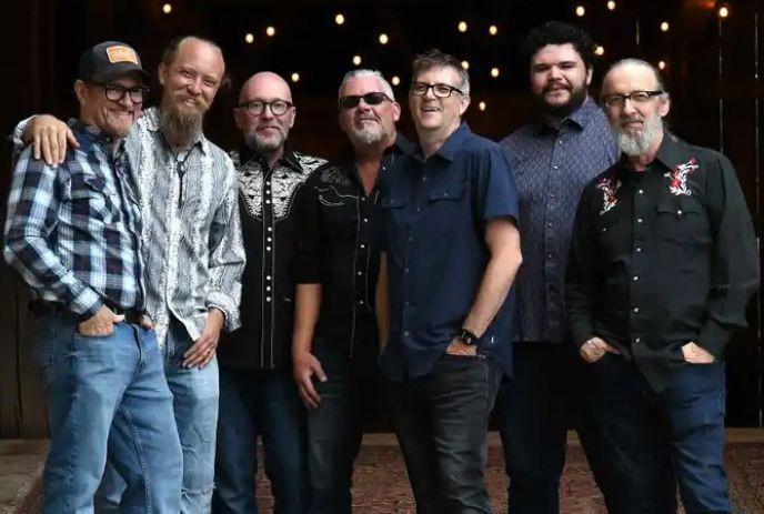 Seven band members from Diamond Mine posing for a picture under a dark background with star lights.
