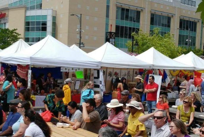 Crowded street fest in a sunny day with food tents, signs, and people enjoying vibrant city vibes.